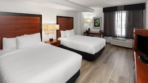 A hotel room with two beds, a desk, a chair, a TV, and a window with curtains.