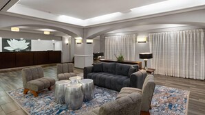 A modern hotel lobby with a reception desk, seating area, and large windows with curtains.