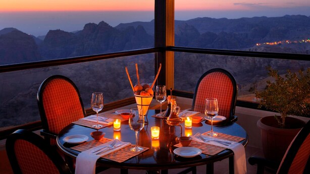 A dining table set for two with a view of mountains at sunset. - Petra Marriott Hotel (Wadi Musa)