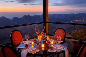 A dining table set for two with a view of mountains at sunset. - Petra Marriott Hotel (Wadi Musa)