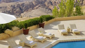 A poolside area with lounge chairs and potted plants, overlooking a mountainous landscape. - Petra Marriott Hotel (Wadi Musa)