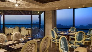 A dining area with tables and chairs, large windows with a view of the mountains, and a ceiling with a patterned design. - Petra Marriott Hotel (Wadi Musa)