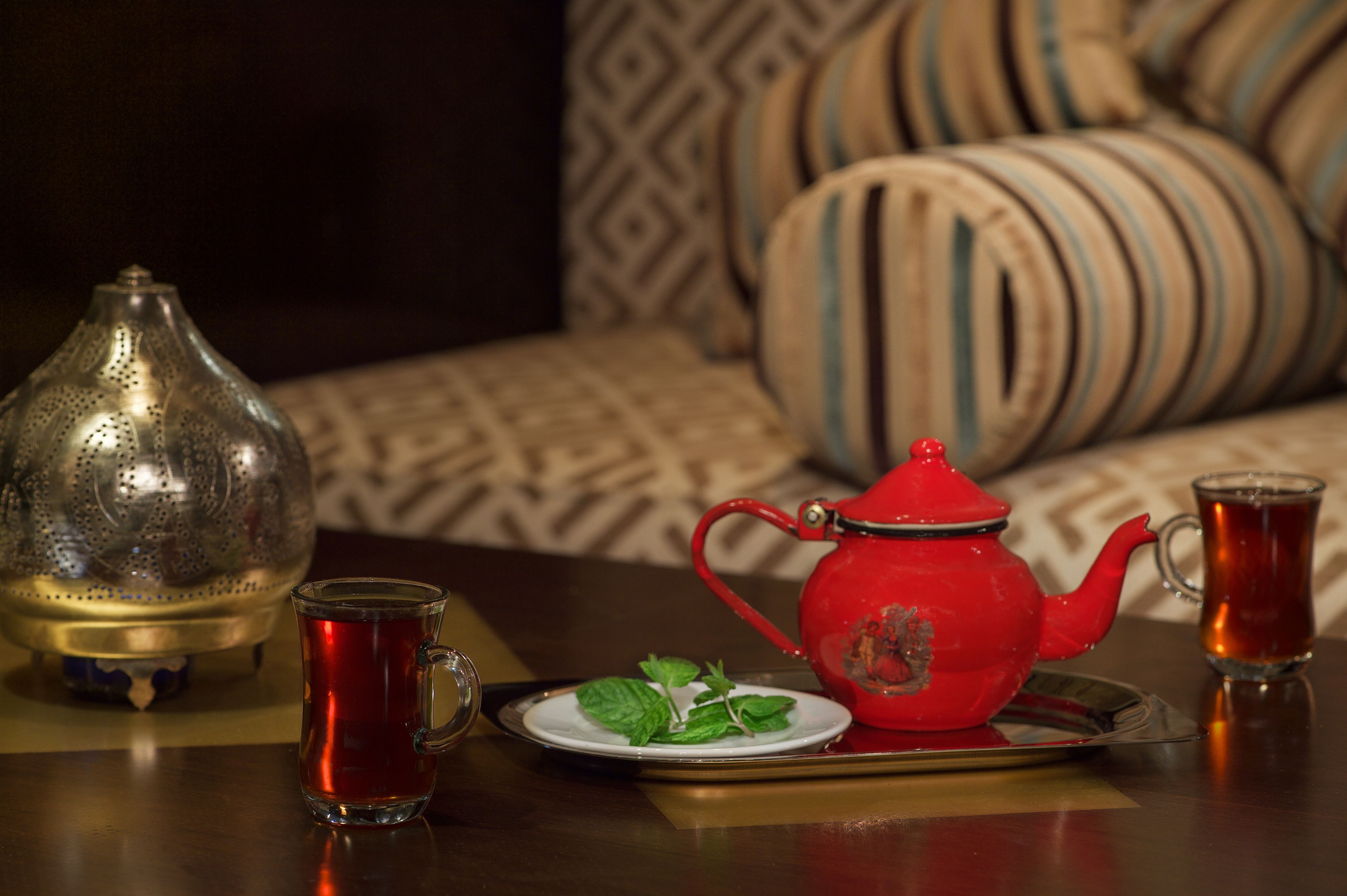 A table with a teapot, two cups, and a tray with a plate of mint leaves.