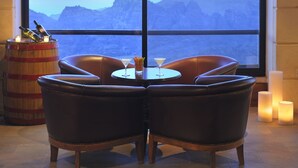 A room with a large window, two leather chairs, a small table with a glass, and candles. - Petra Marriott Hotel (Wadi Musa)