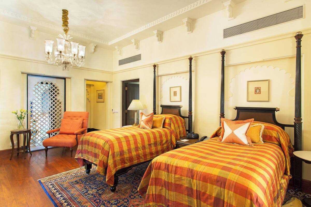 A hotel room with two beds, a sitting area, a chandelier, and a decorative door.