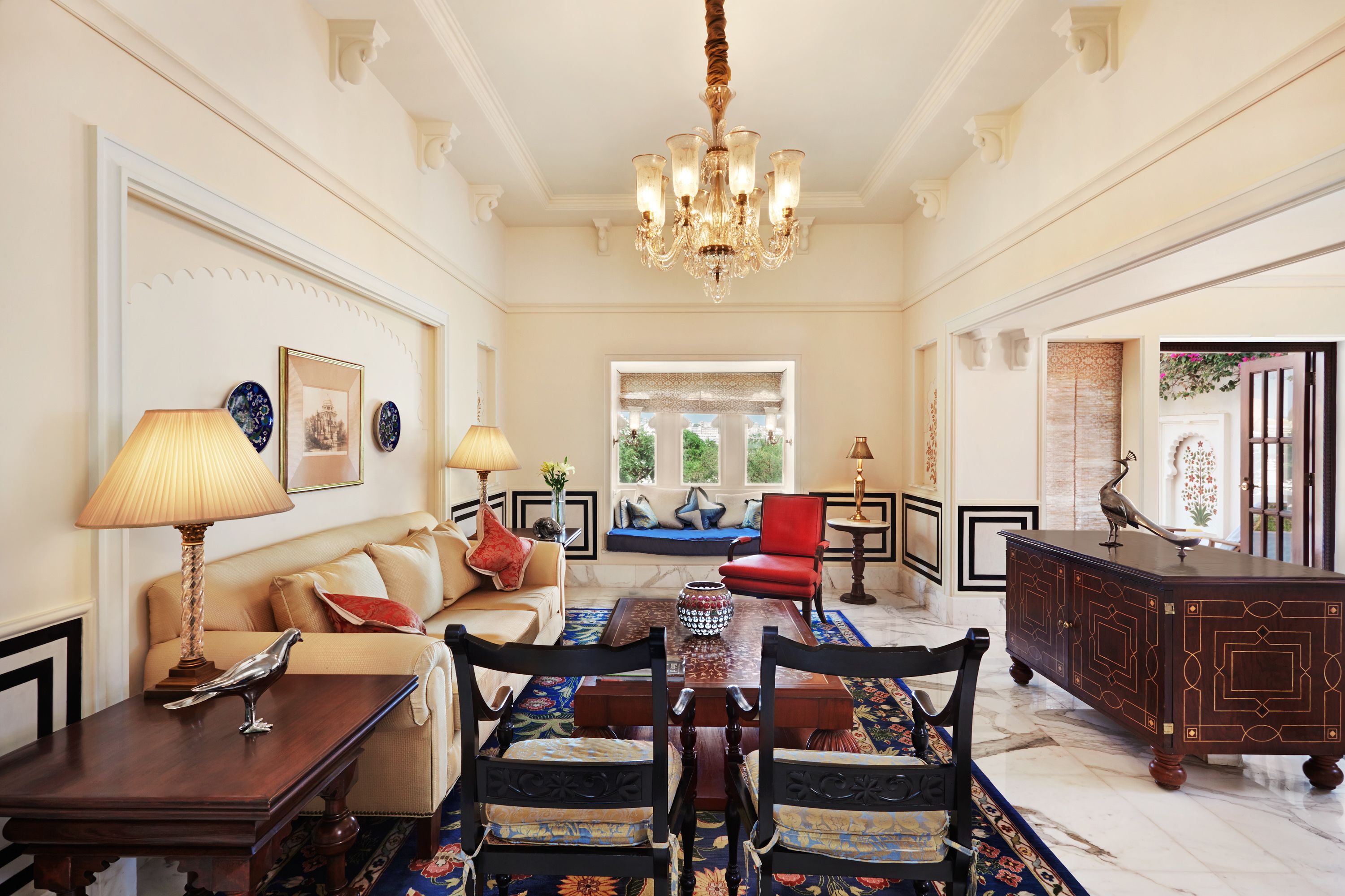 A spacious living room with a chandelier, a sofa set, a dining table, and a decorative cabinet.