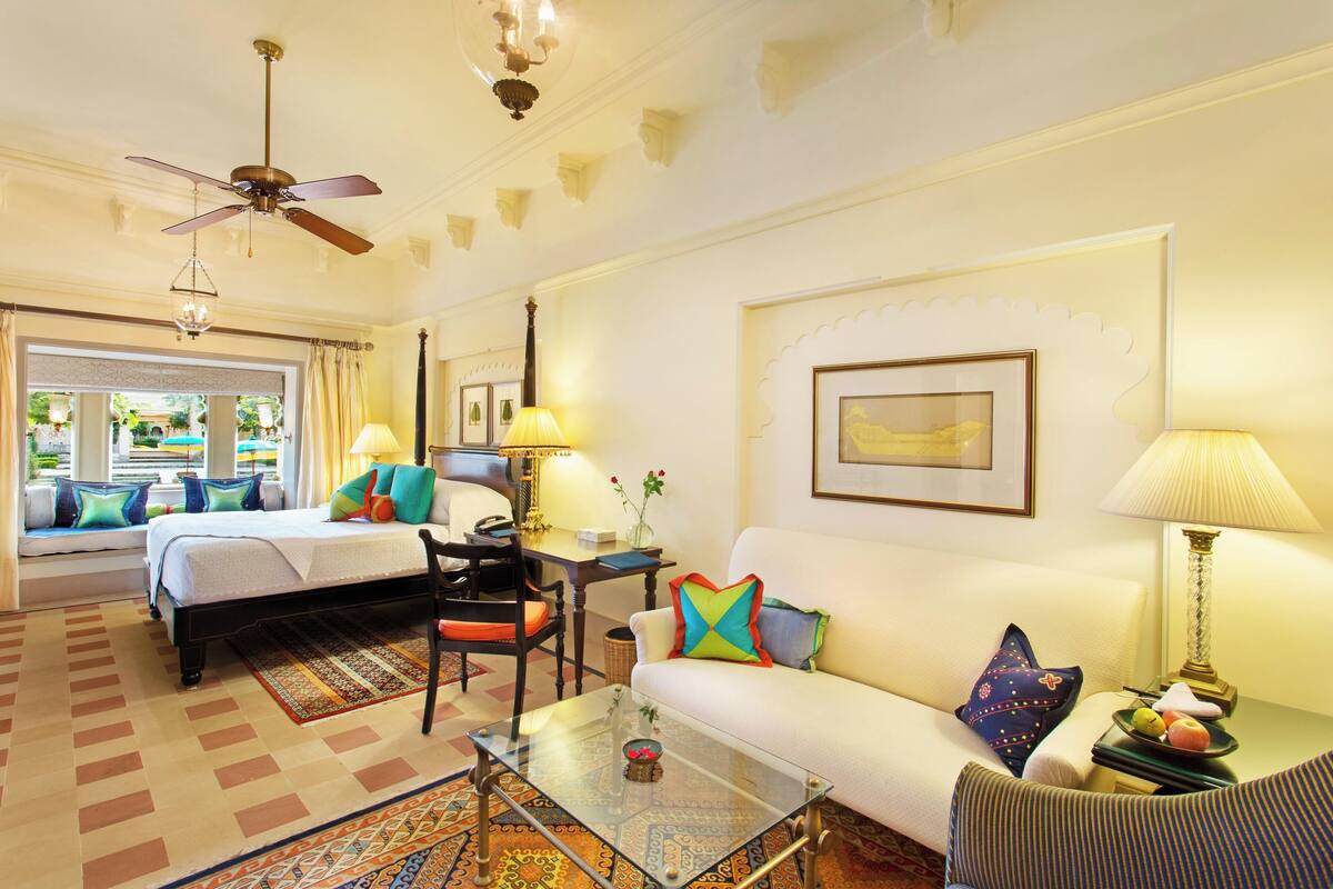 A hotel room with a bed, a sofa, a coffee table, a desk, and a ceiling fan.