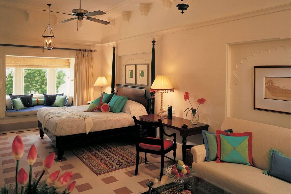 A hotel room with two beds, a sitting area with a sofa, a dining table, and a view of trees through the window.