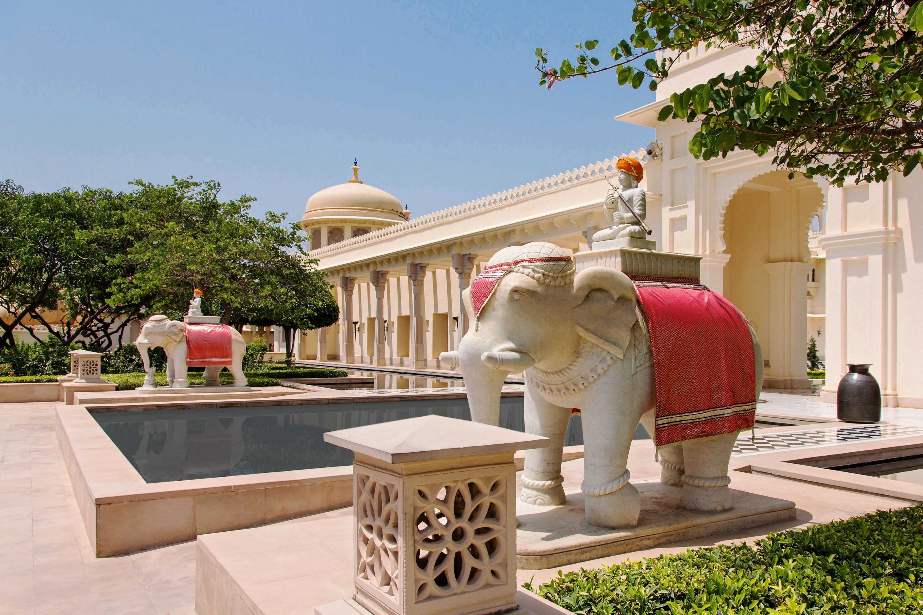 Une cour avec une piscine, une statue représentant une figure à cheval et un bâtiment doté d’arcades et de colonnes.