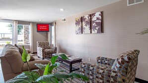 Een hotel lobby met een zithoek, een televisie waarop staat 'Gratis Wi-Fi in alle kamers', en een groot raam met uitzicht op palmbomen.