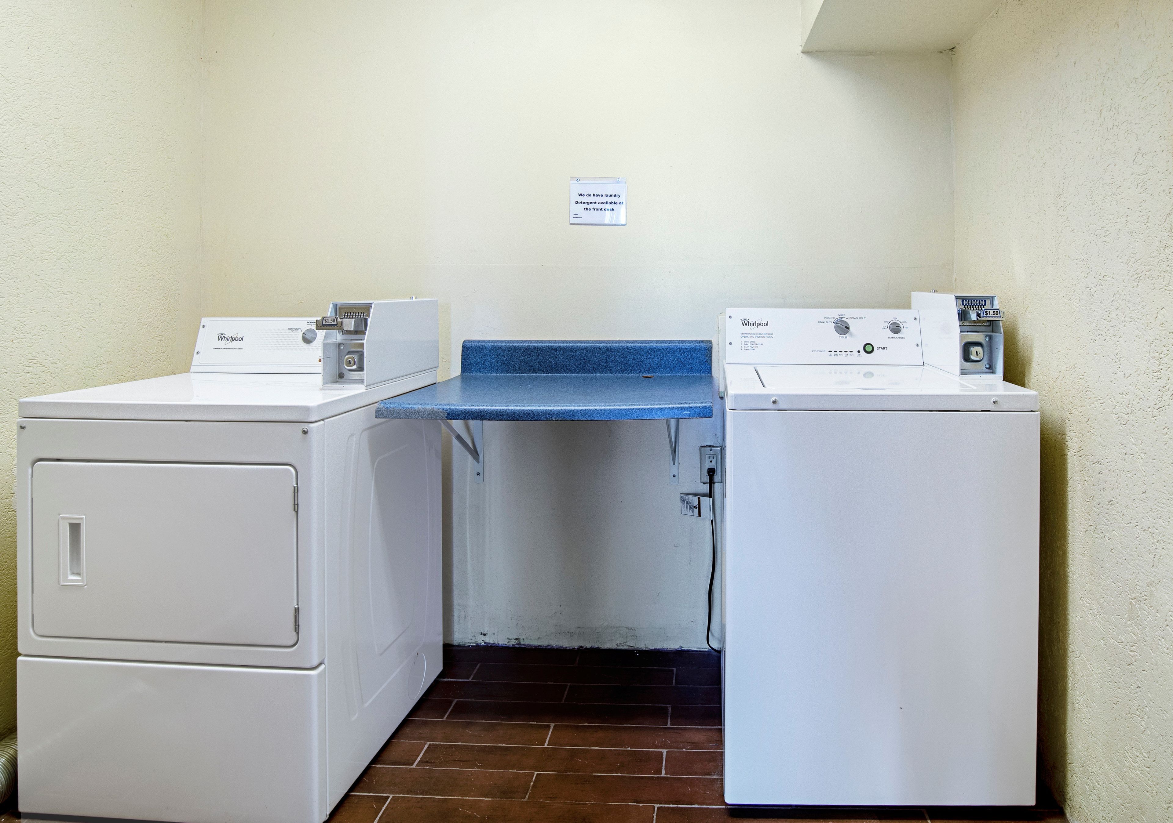 Un lavadero con dos lavadoras Whirlpool y un cartel que indica que hay detergente disponible en la recepción.