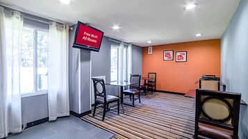 Habitación de hotel con televisor de pantalla plana mostrando 'Wi-Fi gratis en todas las habitaciones', zona de comedor con sillas y mesas, y piso alfombrado.
