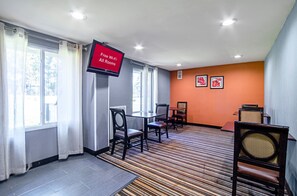 Ein Hotelzimmer mit einem Flachbildfernseher, der 'Kostenloses WLAN in allen Zimmern' anzeigt, einem Essbereich mit Stühlen und Tischen sowie einem Teppichboden.