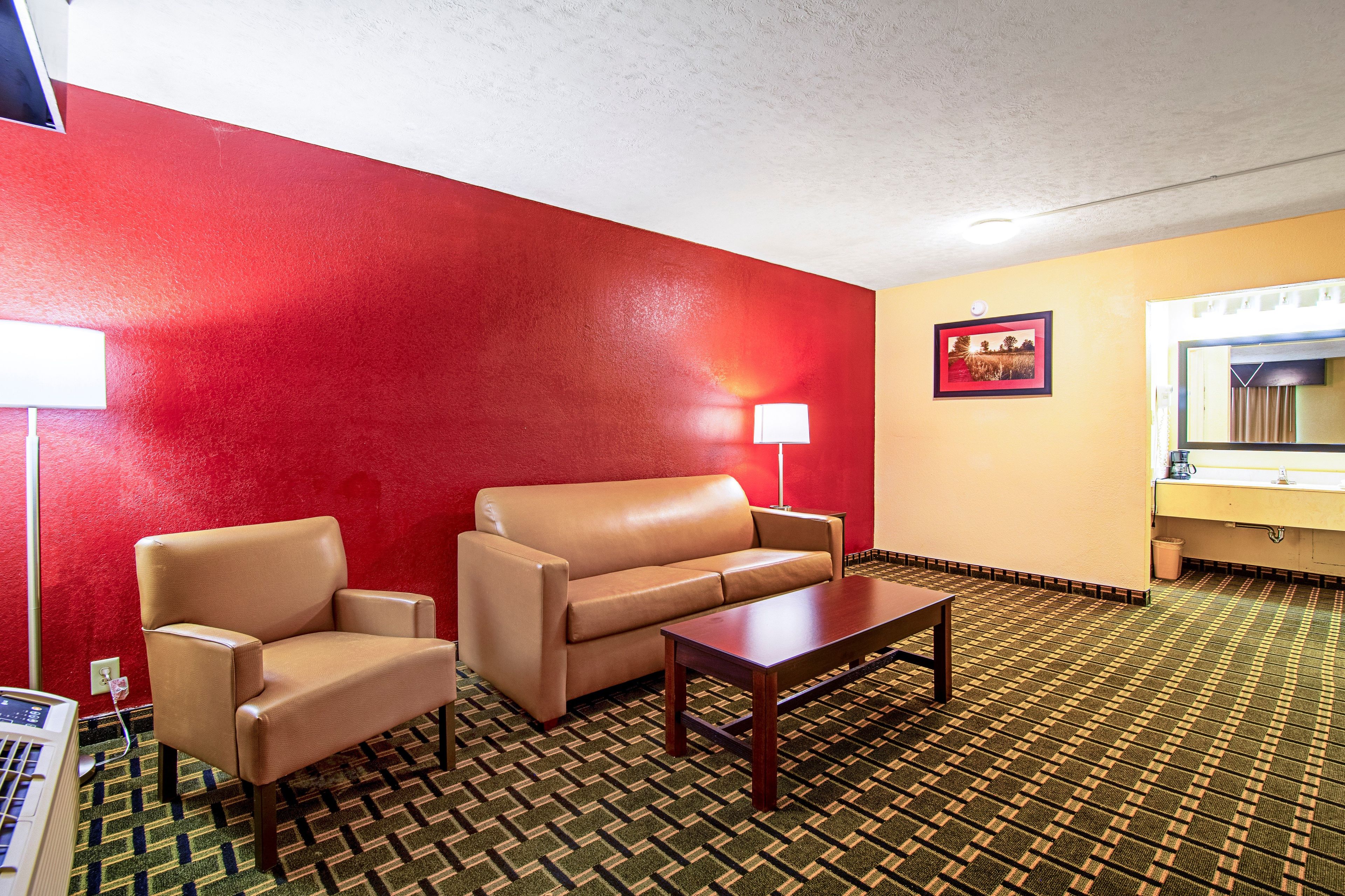 Habitación de hotel con pared roja, sofá color beige, mesa de centro de madera, lámpara y un cuadro enmarcado en la pared.