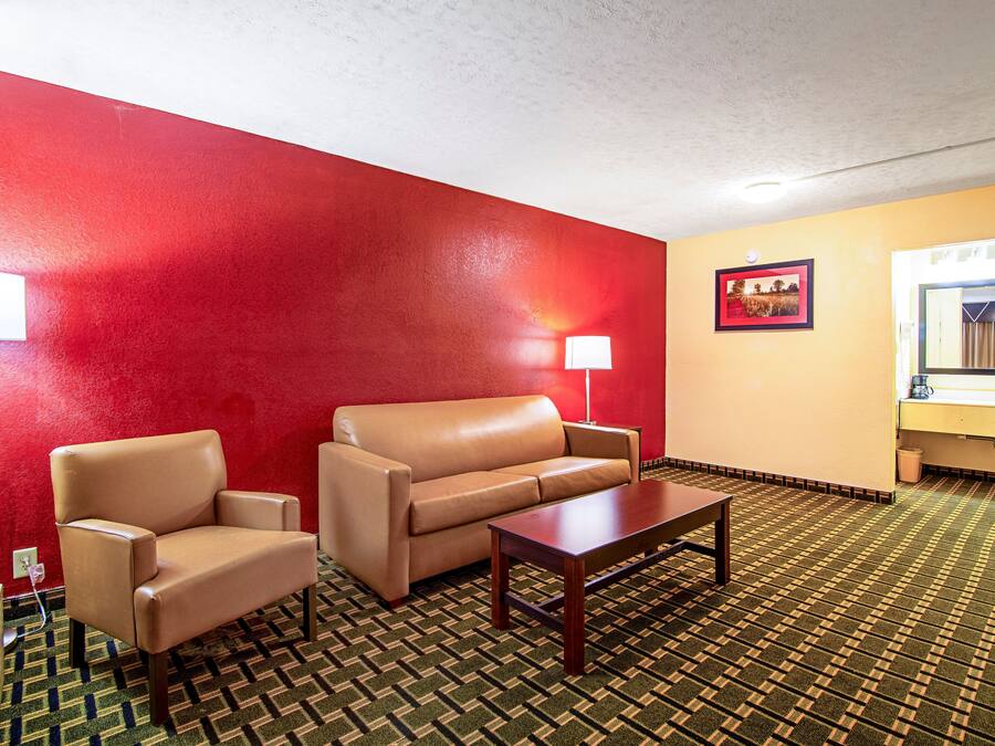 Een hotelkamer met een rode wand, een beige bank, een houten bijzettafeltje, een lamp en een lijst met een afbeelding aan de muur.
