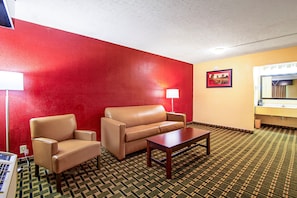 Une chambre d’hôtel avec un mur rouge, un canapé beige, une table basse en bois, une lampe et un tableau encadré accroché au mur.