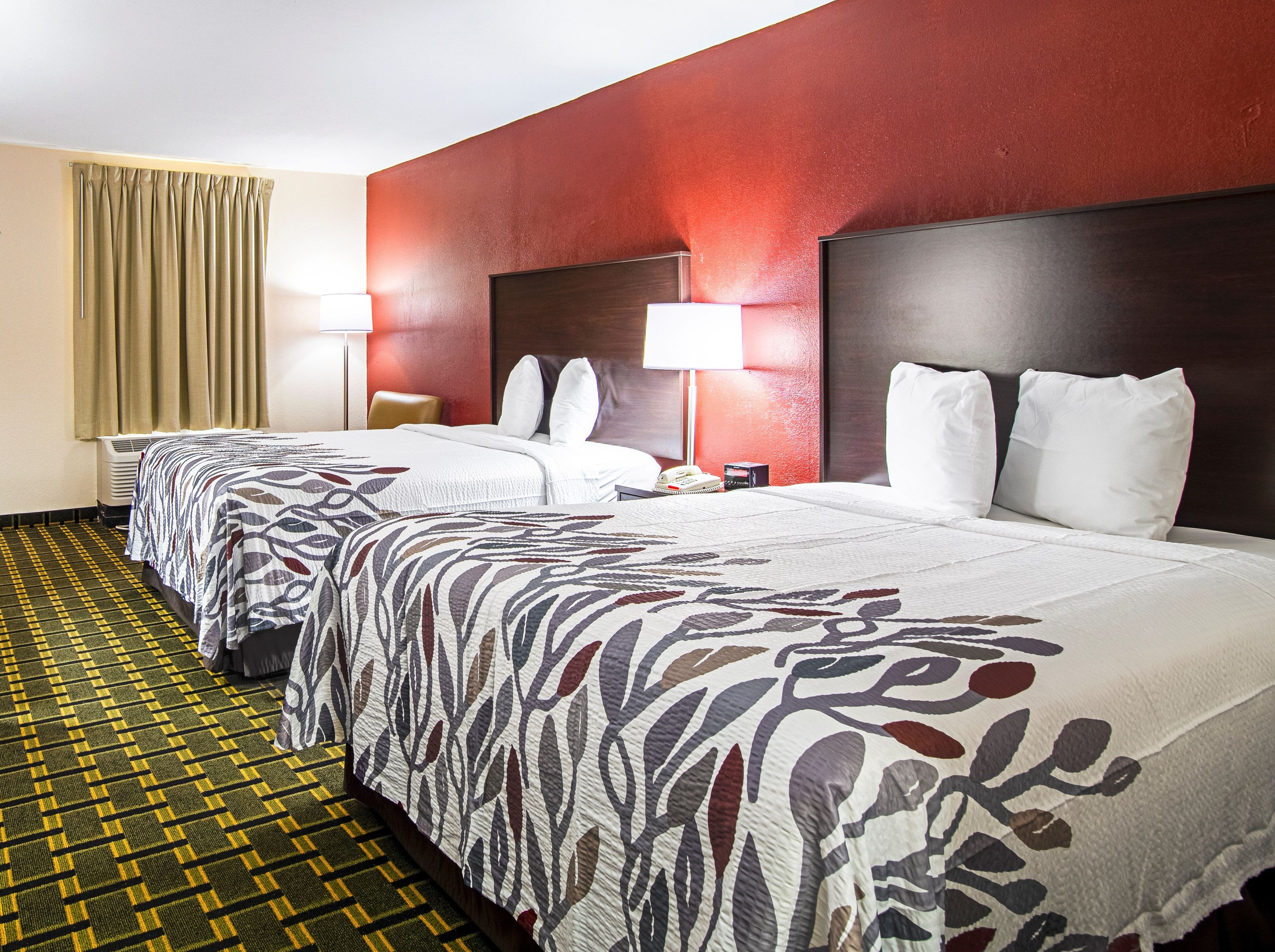 Ein Hotelzimmer mit zwei Betten, einer roten Wand und einem gemusterten Teppich.