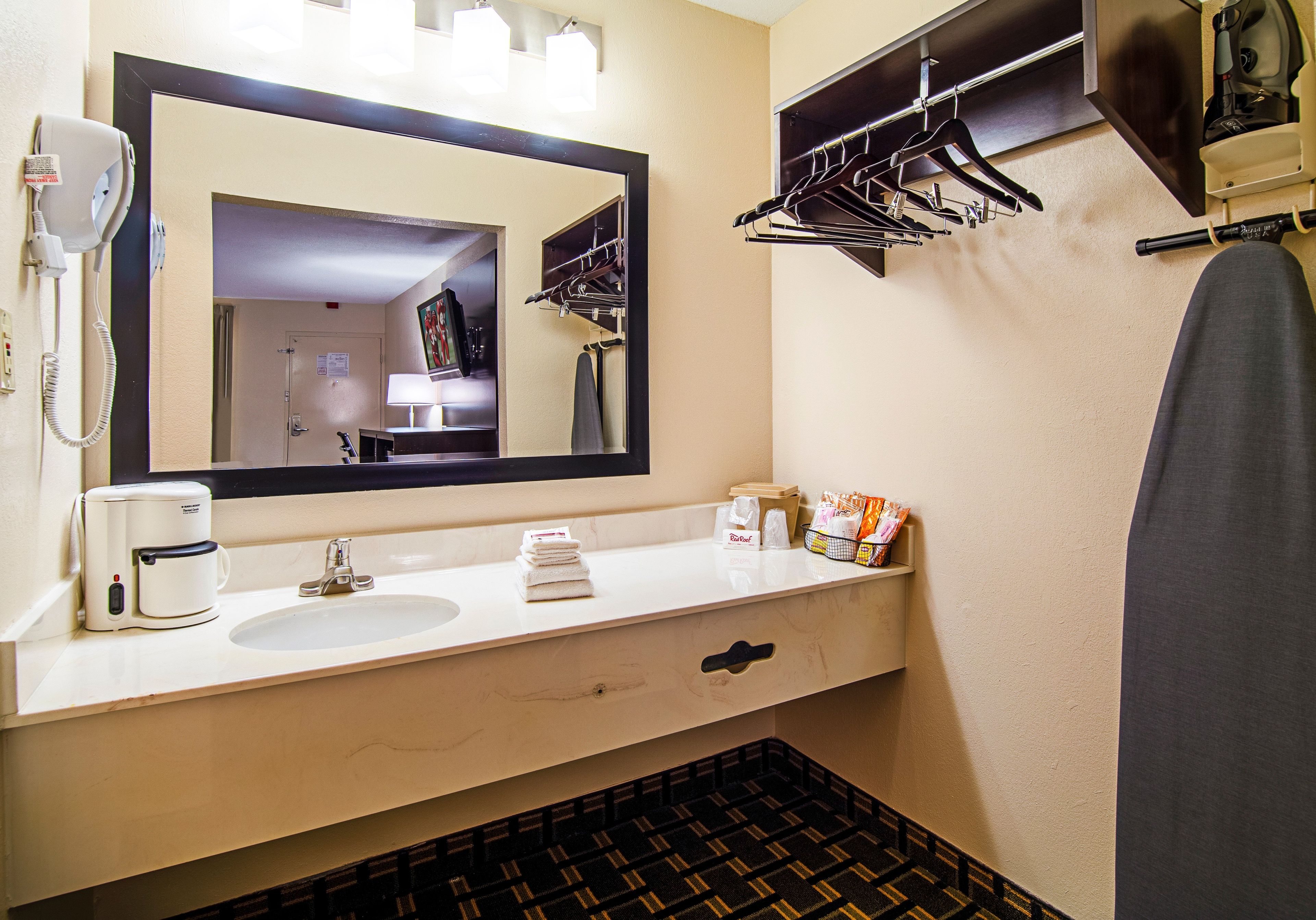 A hotel bathroom with a sink, mirror, towel rack, and a shower area.