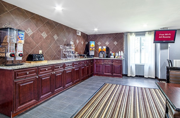A modern kitchen with a marble countertop, built-in cabinets, a coffee machine, and a flat-screen TV displaying "Free Wi-Fi All Rooms". - Red Roof Inn & Suites Greenwood, SC (Greenwood)