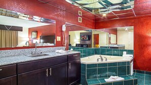 A hotel bathroom with a large mirror, a sink, a hairdryer, a bathtub, and a vanity with a mirror. - Red Roof Inn & Suites Greenwood, SC (Greenwood)