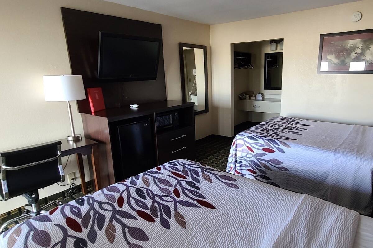 Een hotelkamer met twee bedden, een televisie, een bureau met lamp, een dressoir en een spiegel.