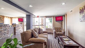 A lobby with a stone wall, a reception desk, a sofa, a patterned armchair, and a television screen displaying 'Free Wi-Fi All Rooms'. - Red Roof Inn & Suites Greenwood, SC (Greenwood)