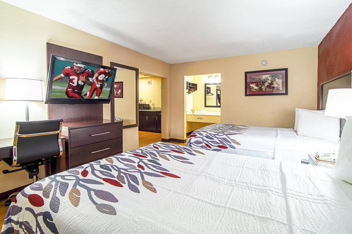 Ein Hotelzimmer mit zwei Betten, einem Fernseher, einem Schreibtisch und einem durchgegangenen Tür erkennbaren Badezimmer.
