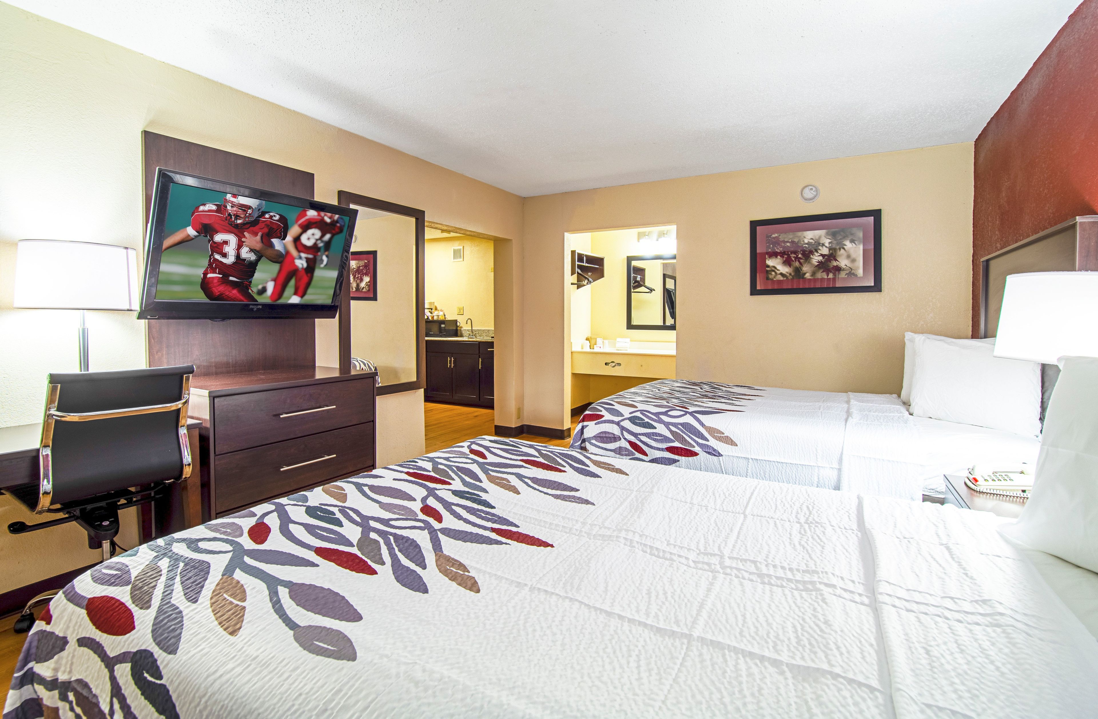 Una habitación de hotel con dos camas, televisión, escritorio y kitchenette.