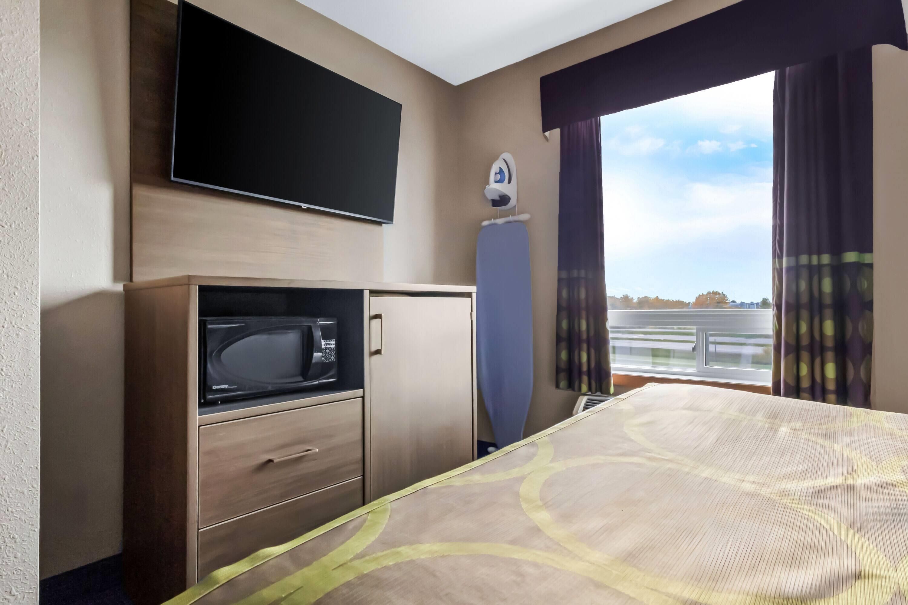 Habitación de hotel con cama, televisión montada en la pared, microondas y una plancha pequeña.