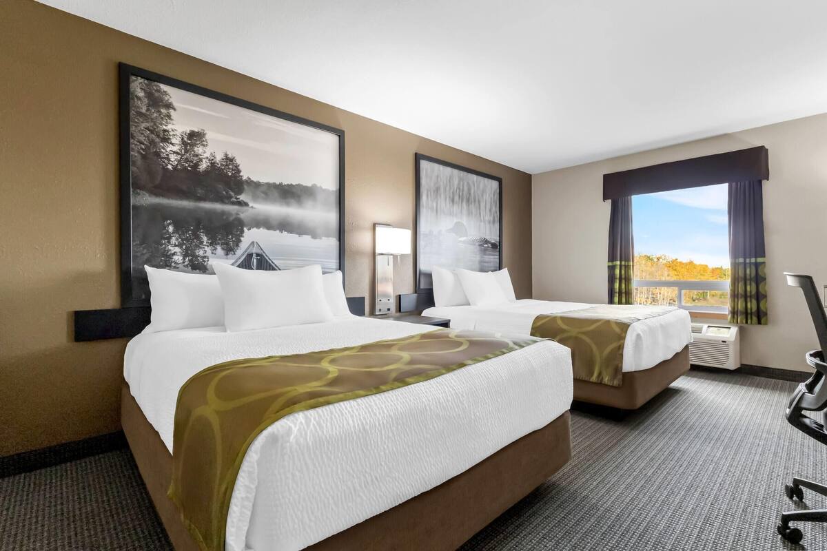 A hotel room with two beds, a desk, a chair, and a large window with a view.