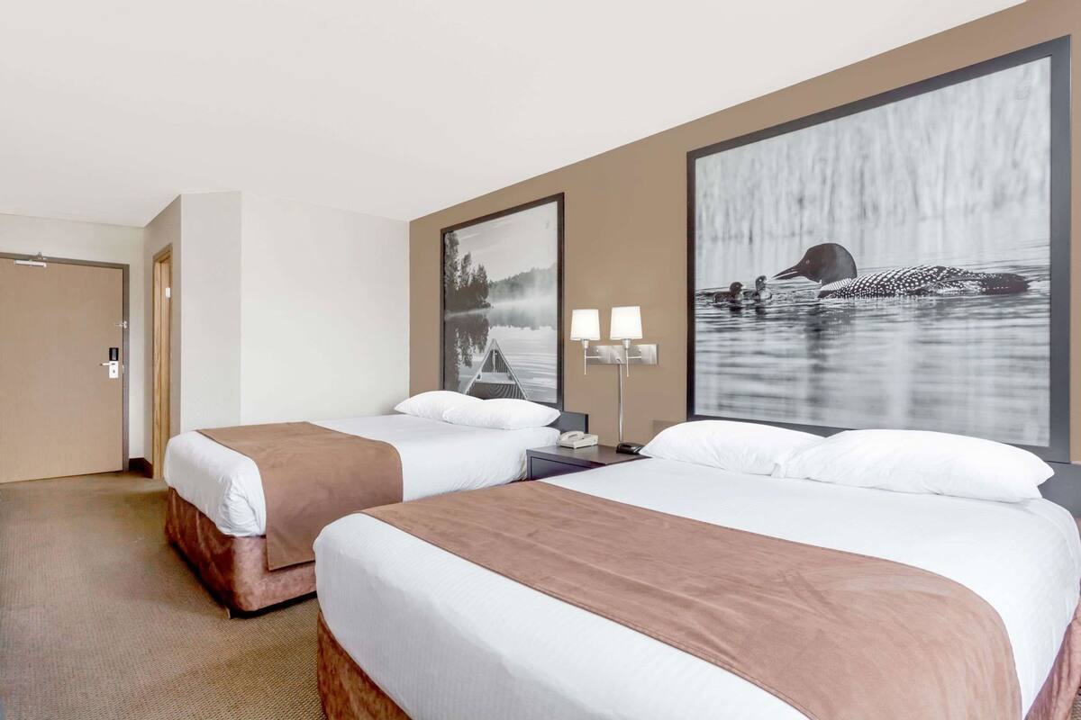 A hotel room with two beds, a large window, and a wall-mounted lamp.