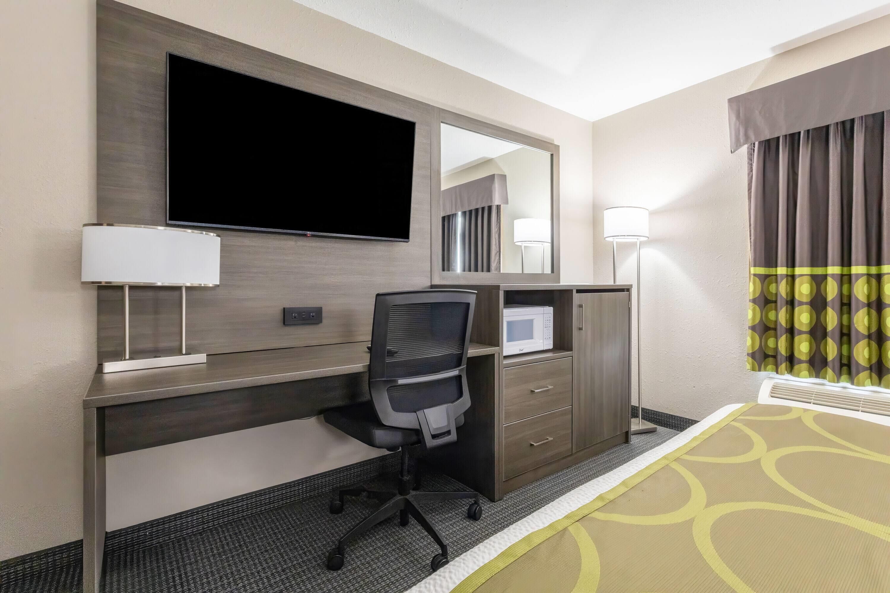 A hotel room with a desk, chair, television, and a bed with a patterned bedspread.