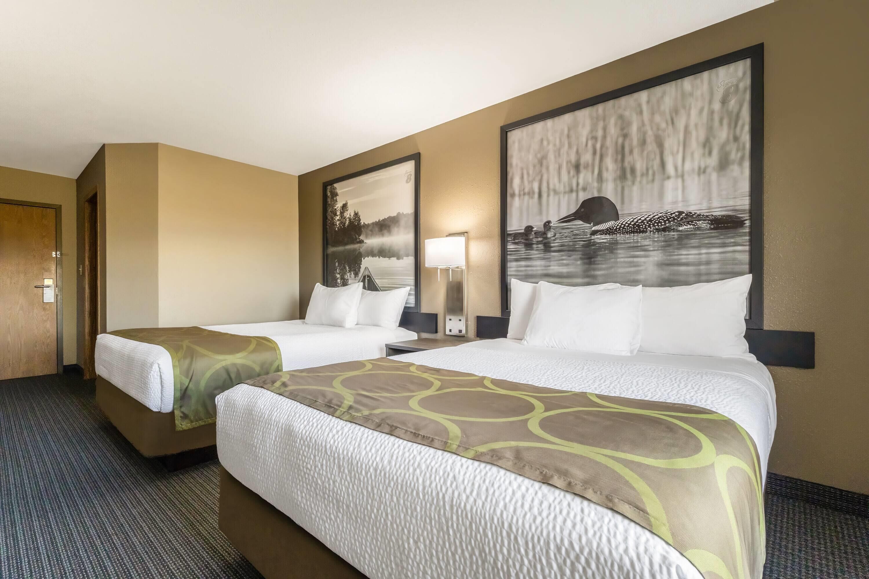 A hotel room with two beds, a large window with a view of a lake, and a painting of a bear on the wall.