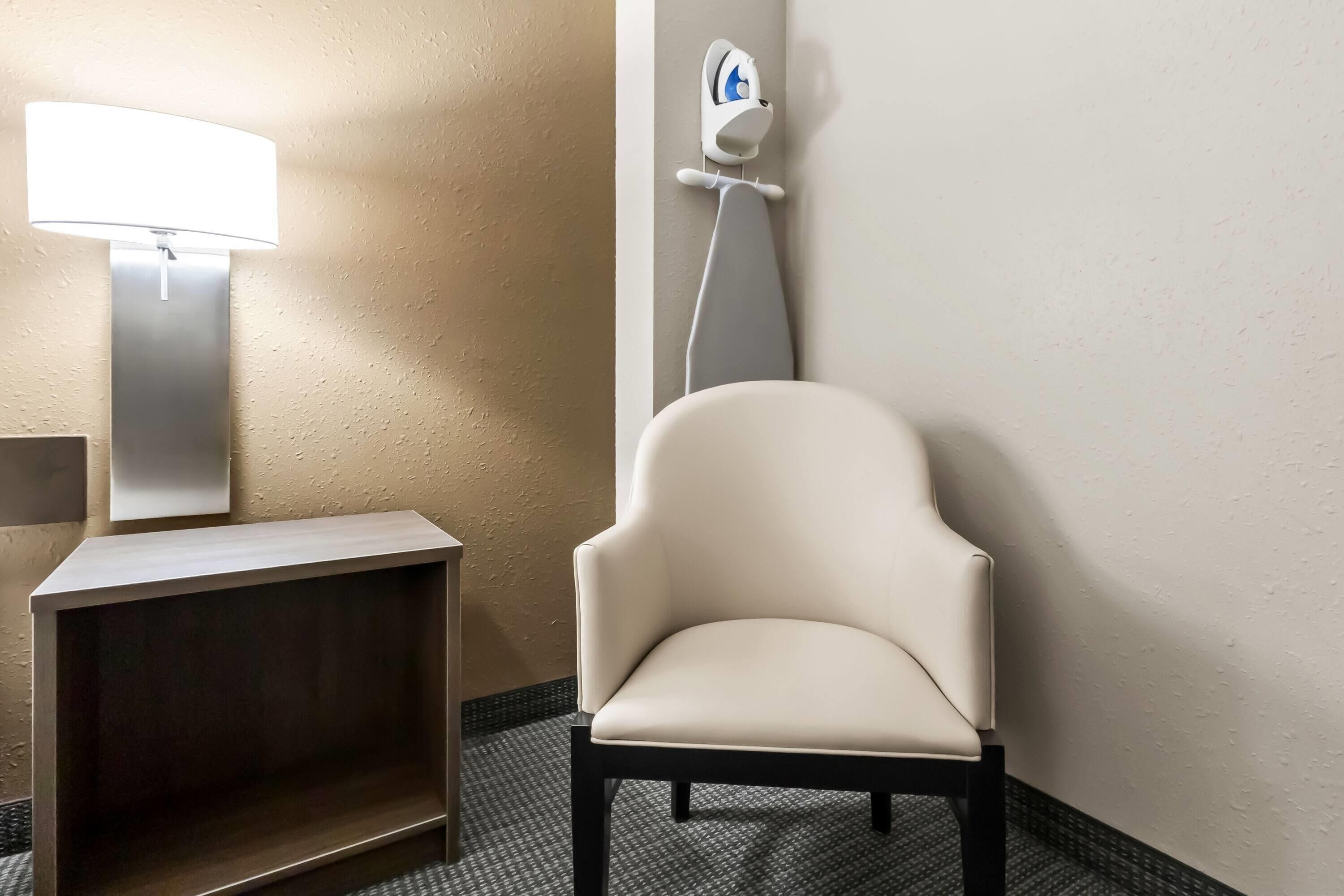 Une salle de bain avec une chaise blanche, un distributeur de papier toilette fixé au mur et un lampadaire.