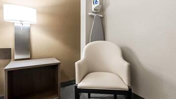 Une salle de bain avec une chaise blanche, un distributeur de papier toilette fixé au mur et un lampadaire.