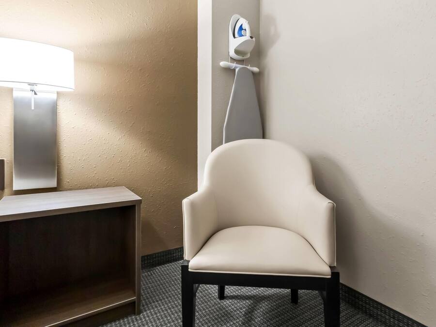 Une salle de bain avec une chaise blanche, un distributeur de papier toilette fixé au mur et un lampadaire.