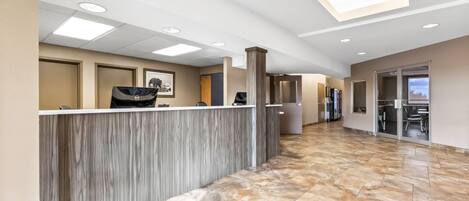 A hotel reception area with a marble floor, a reception desk, and a view of the lobby.