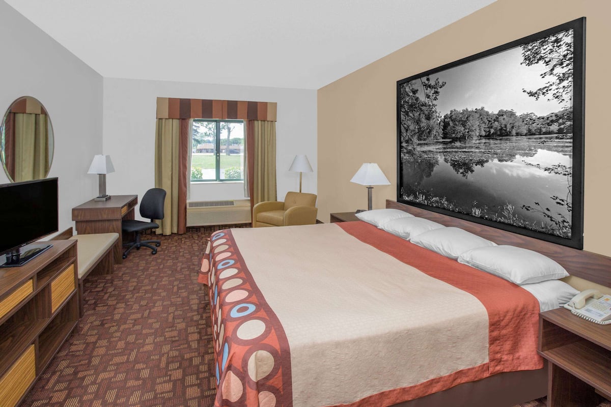 Una habitación de hotel con cama, escritorio, silla, televisor y un amplio ventanal con cortinas.