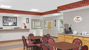 Espaço de café da manhã de hotel com mesas, cadeiras e um balcão com máquina de café, e uma placa com a inscrição 'Superstart breakfast'.