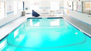 Uma grande piscina coberta com água azul cristalina, rodeada por paredes brancas e detalhes azuis.