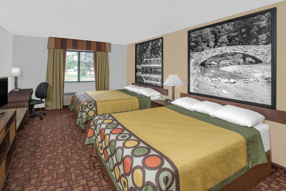 Habitación de hotel con dos camas, un escritorio, una silla, un televisor y un ventanal con cortinas.