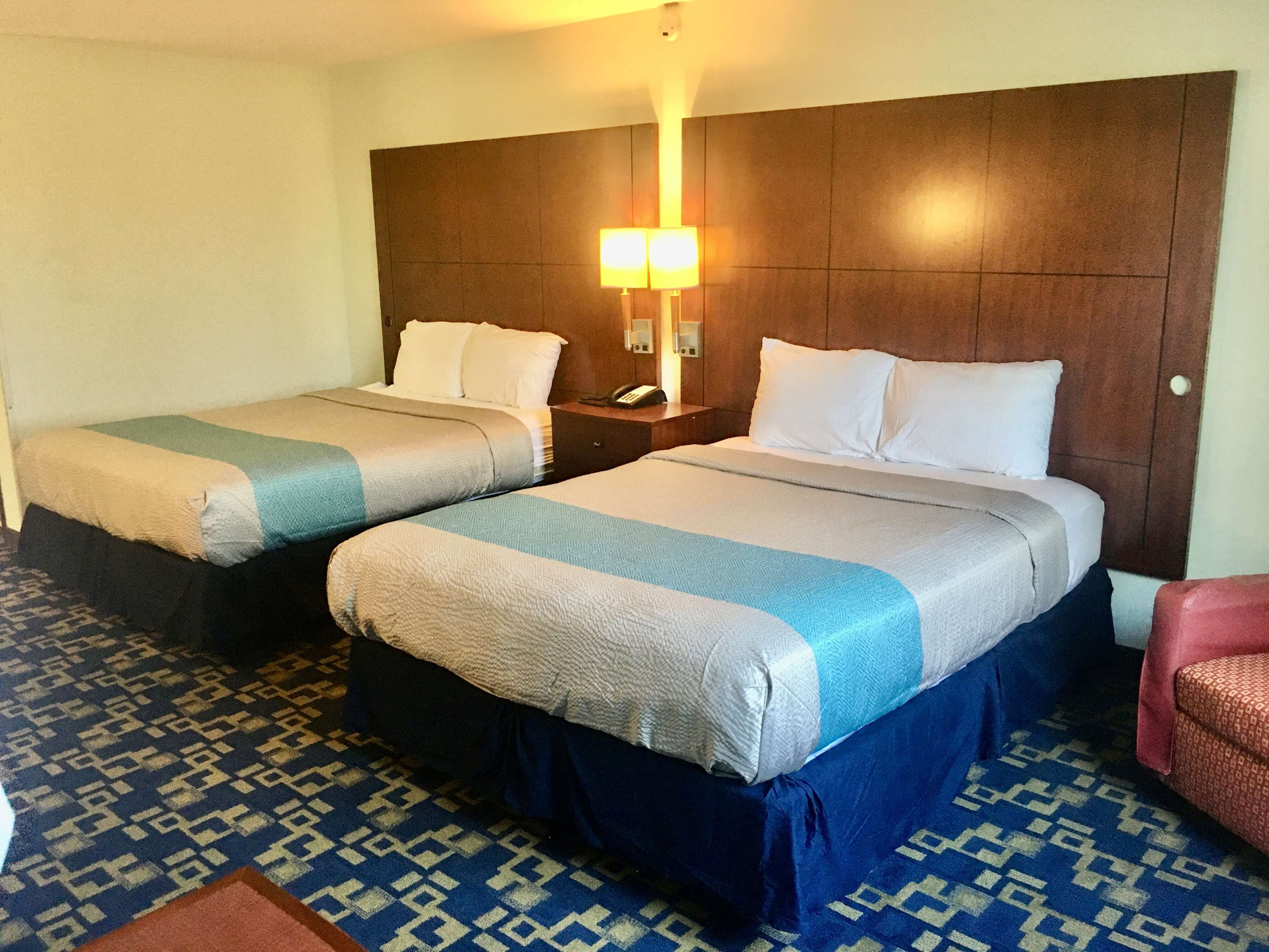 A hotel room with two beds, a nightstand with a lamp, and patterned carpeting.