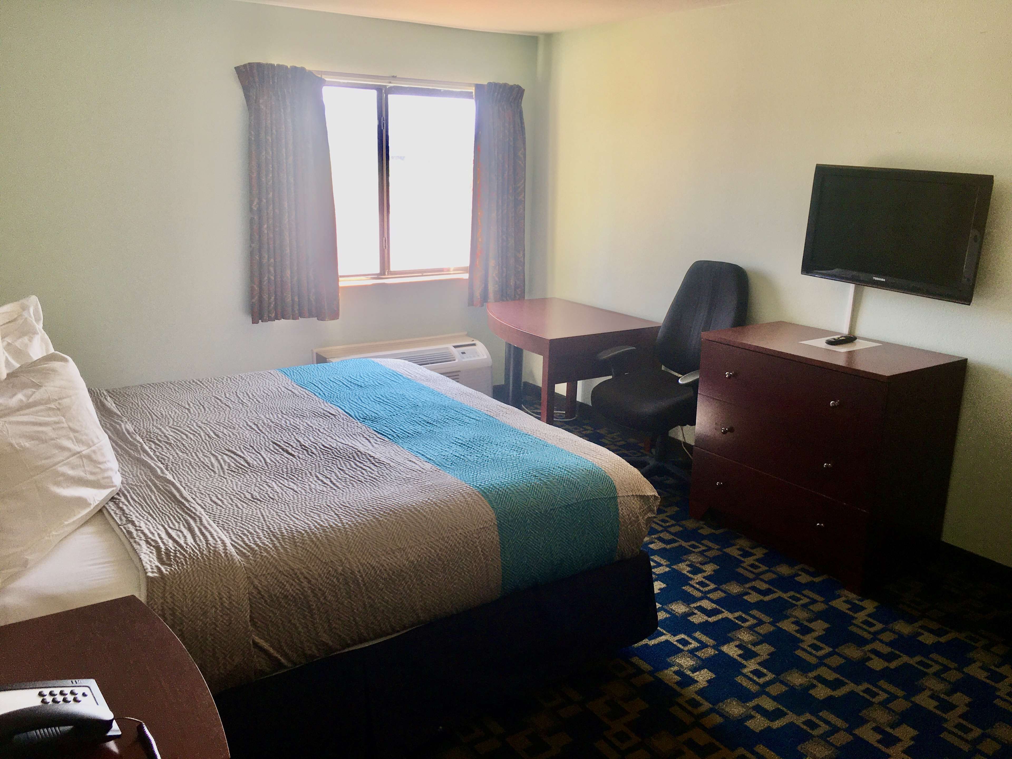 Hotelkamer met een bed, bureau, stoel, dressoir, televisie en raam met gordijnen.
