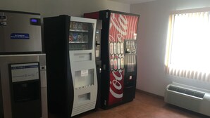 Huoneessa on jääkaappi, Coca-Cola-automaatti ja ikkuna, jossa on sälekaihtimet.