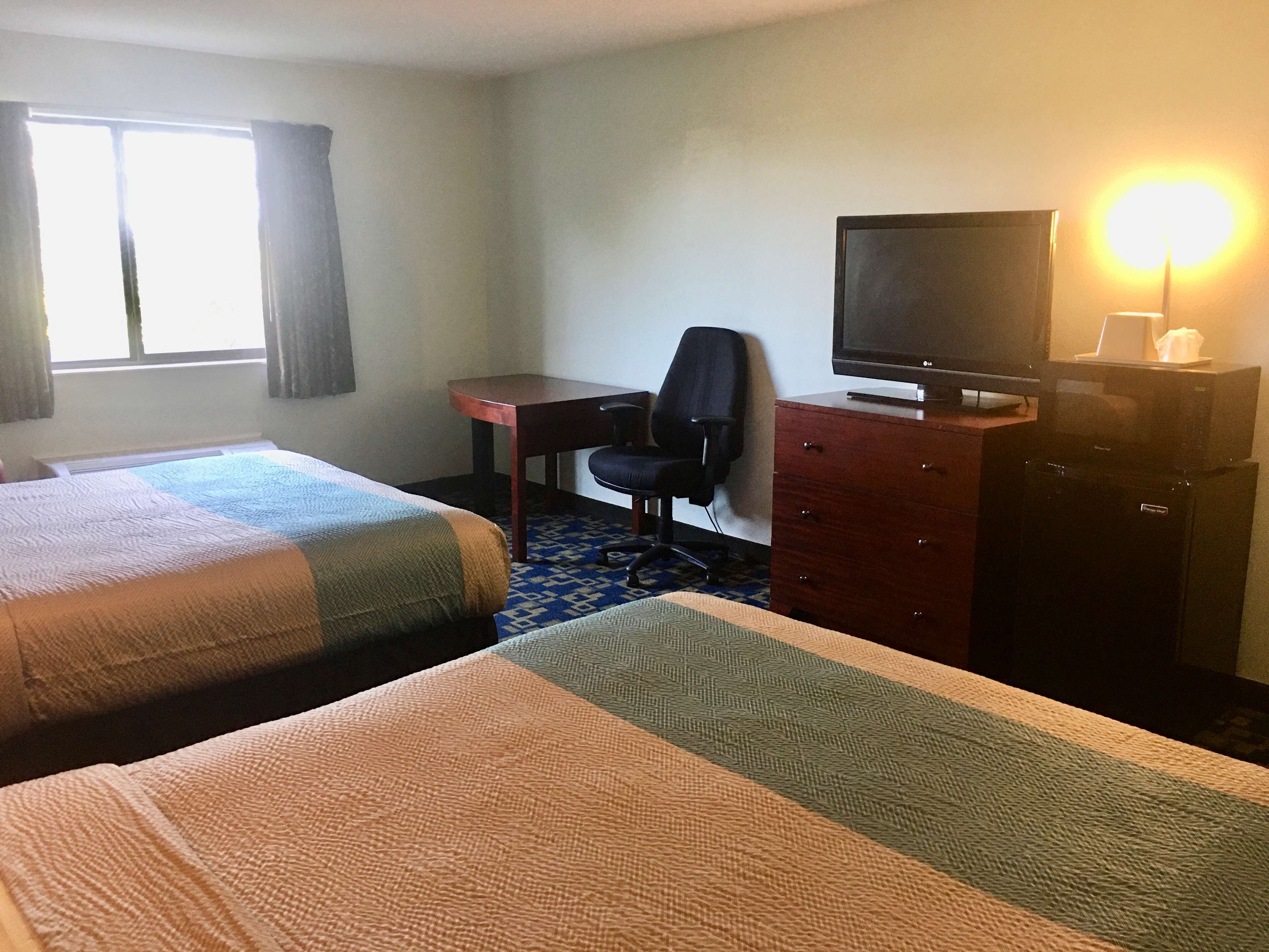 A hotel room with two beds, a desk, a chair, a television, and a dresser.
