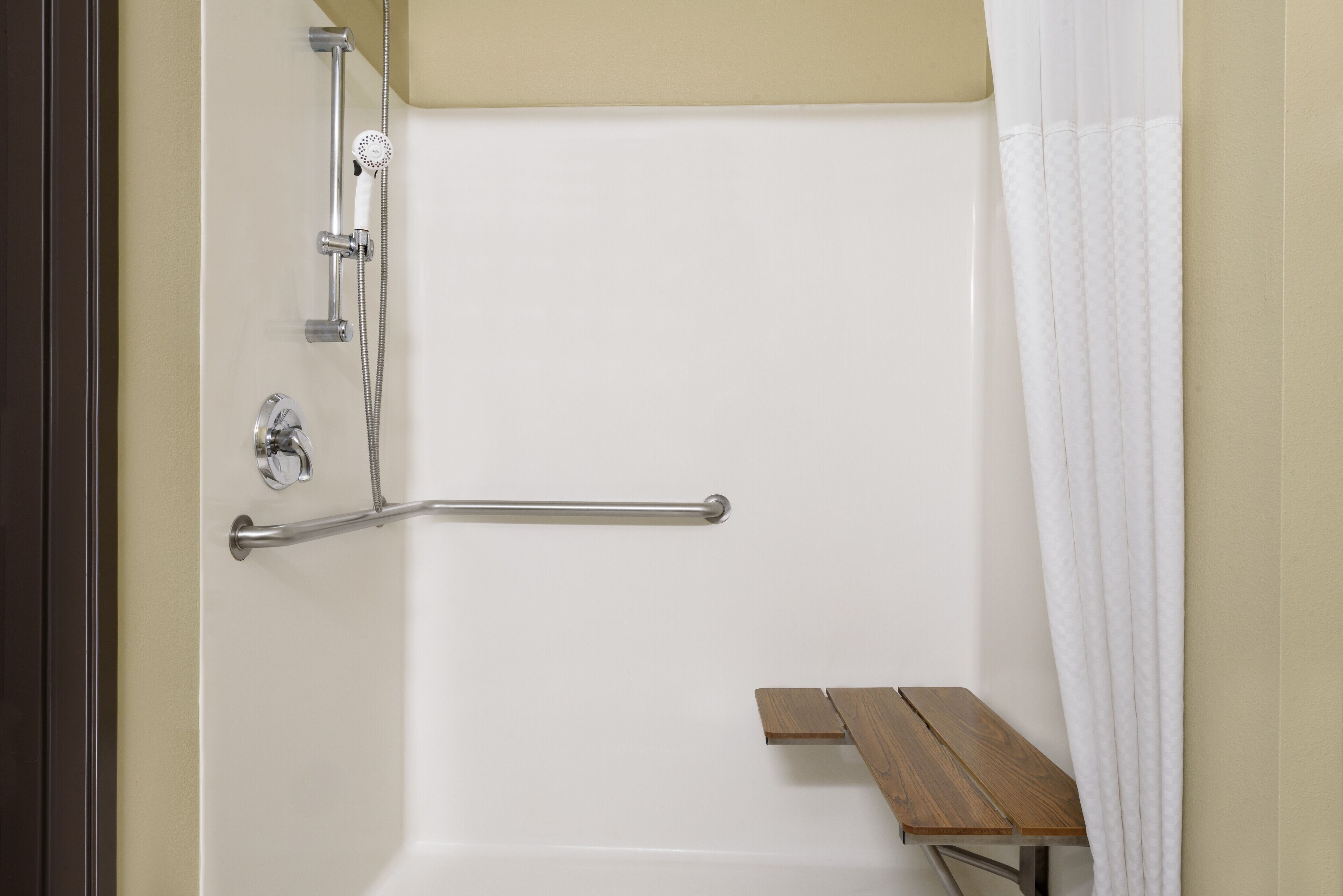 Zona de ducha con barra de apoyo, asiento y cabezal de ducha.