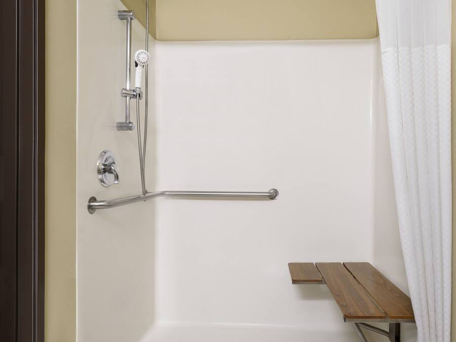 A shower area with a grab bar, a bench, and a showerhead.