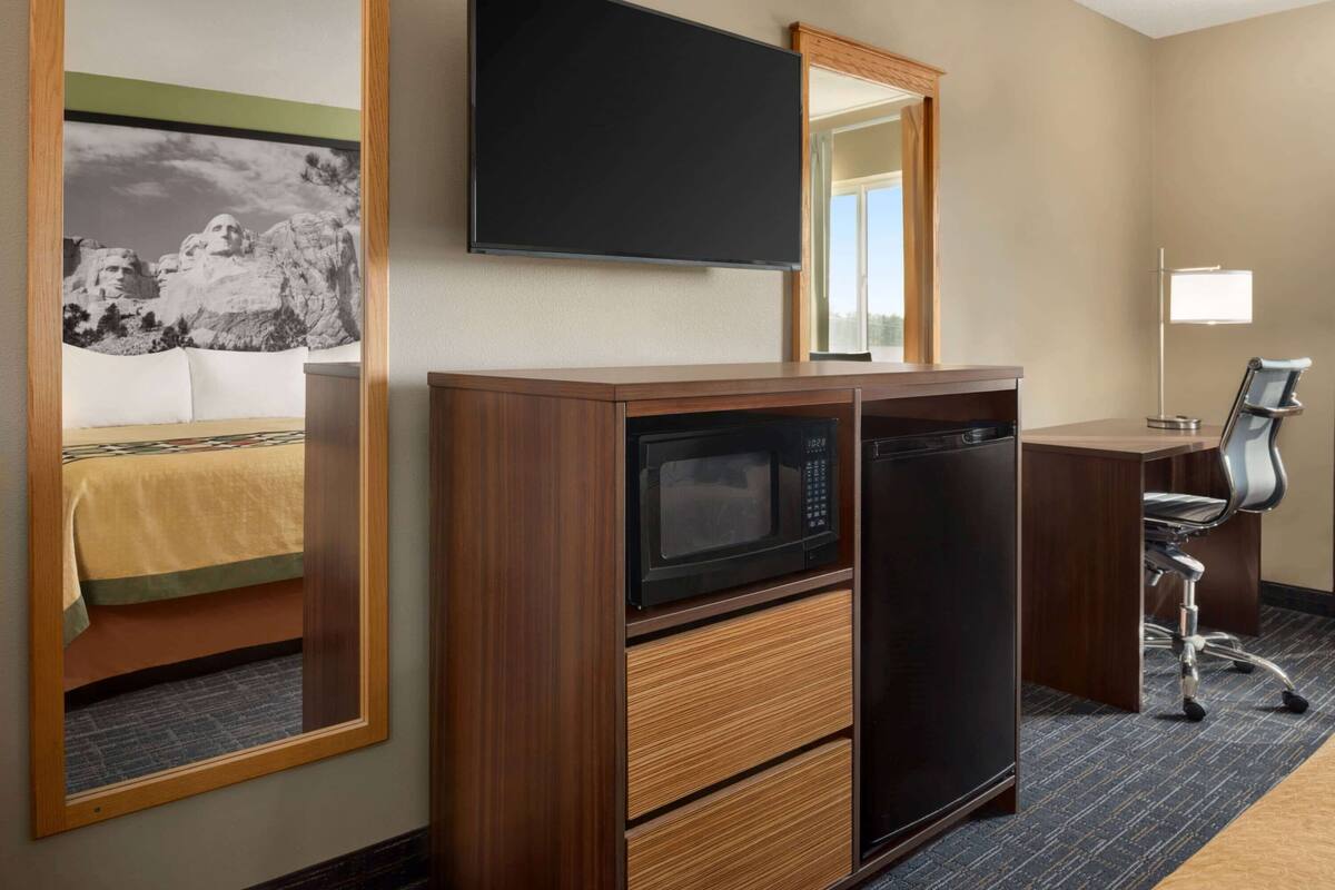 Une chambre d’hôtel avec un bureau en bois, un four à micro-ondes, un réfrigérateur, une chaise et un lit donnant sur une vue sur la montagne.