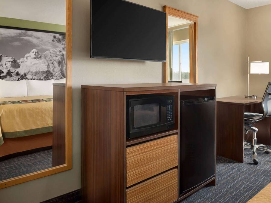 A hotel room with a wooden desk, a microwave, a refrigerator, a chair, and a bed with a view of a mountain.