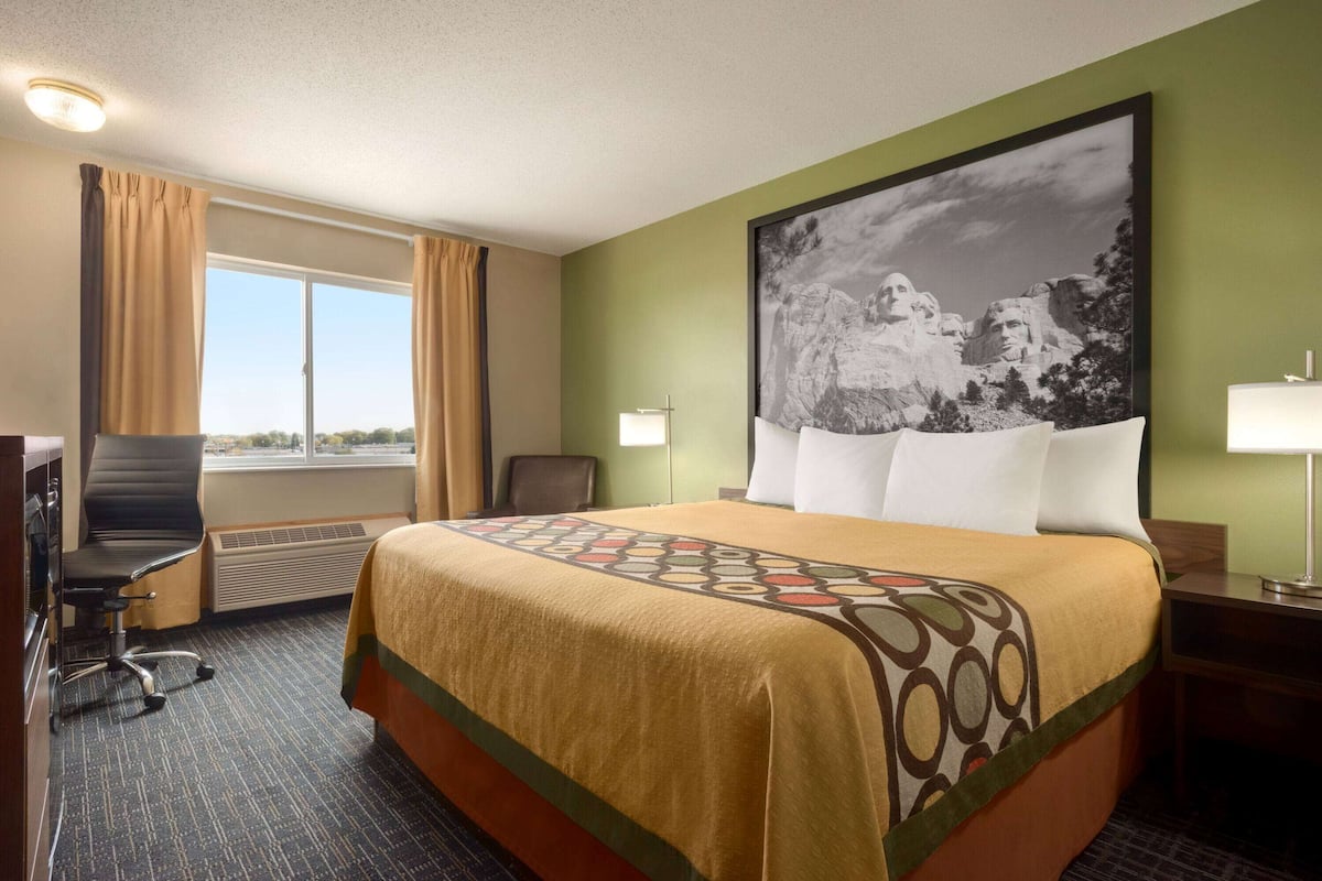 Une chambre d’hôtel avec un grand lit, un bureau, une chaise, une fenêtre avec des rideaux et un tableau au mur.